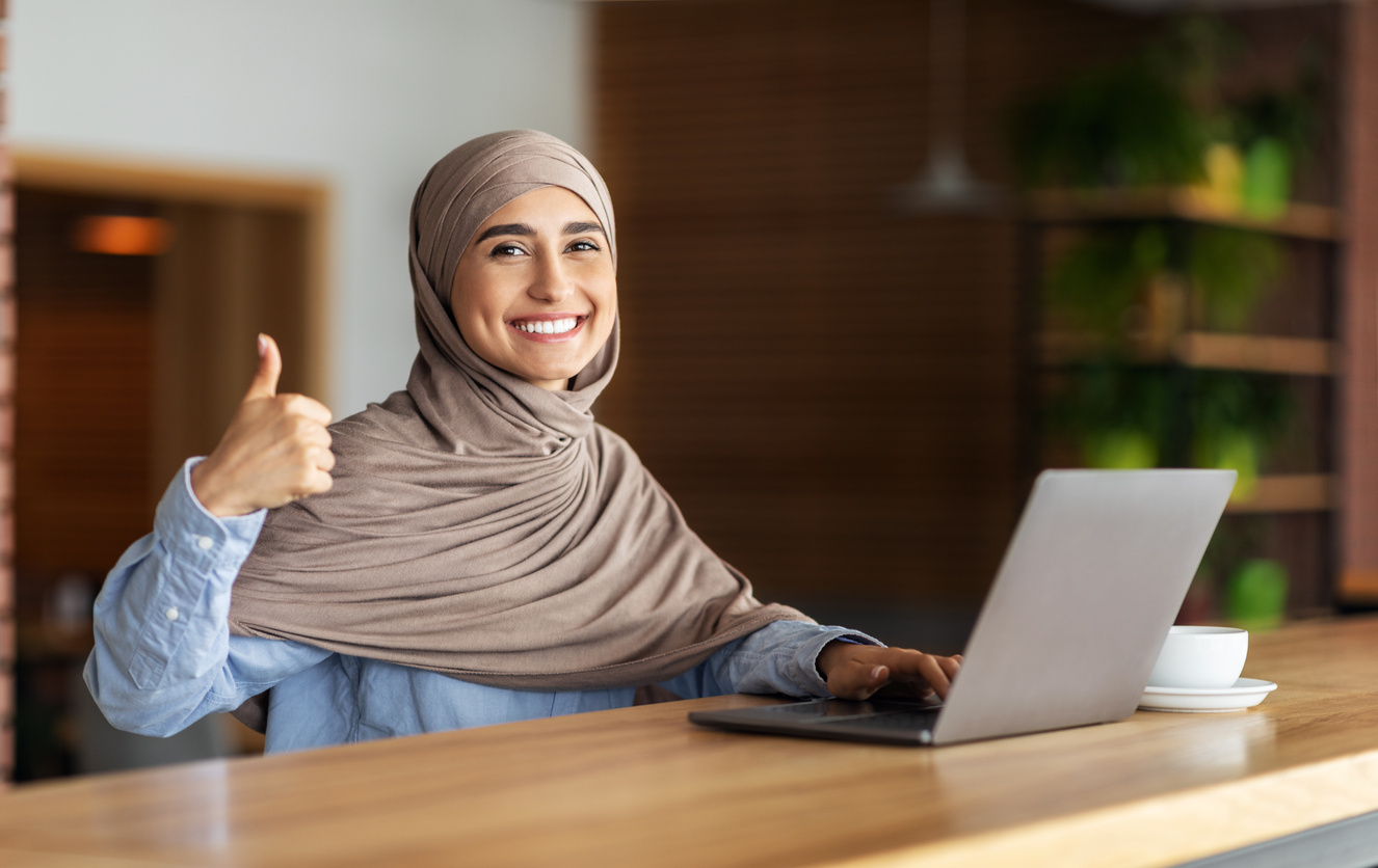 Happy muslim woman in hijab working online at cafe